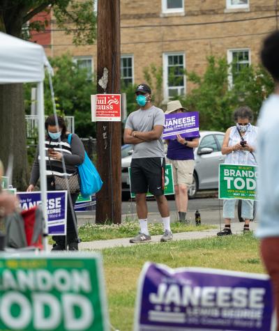 People lined up to vote, some out of focus int he foreground